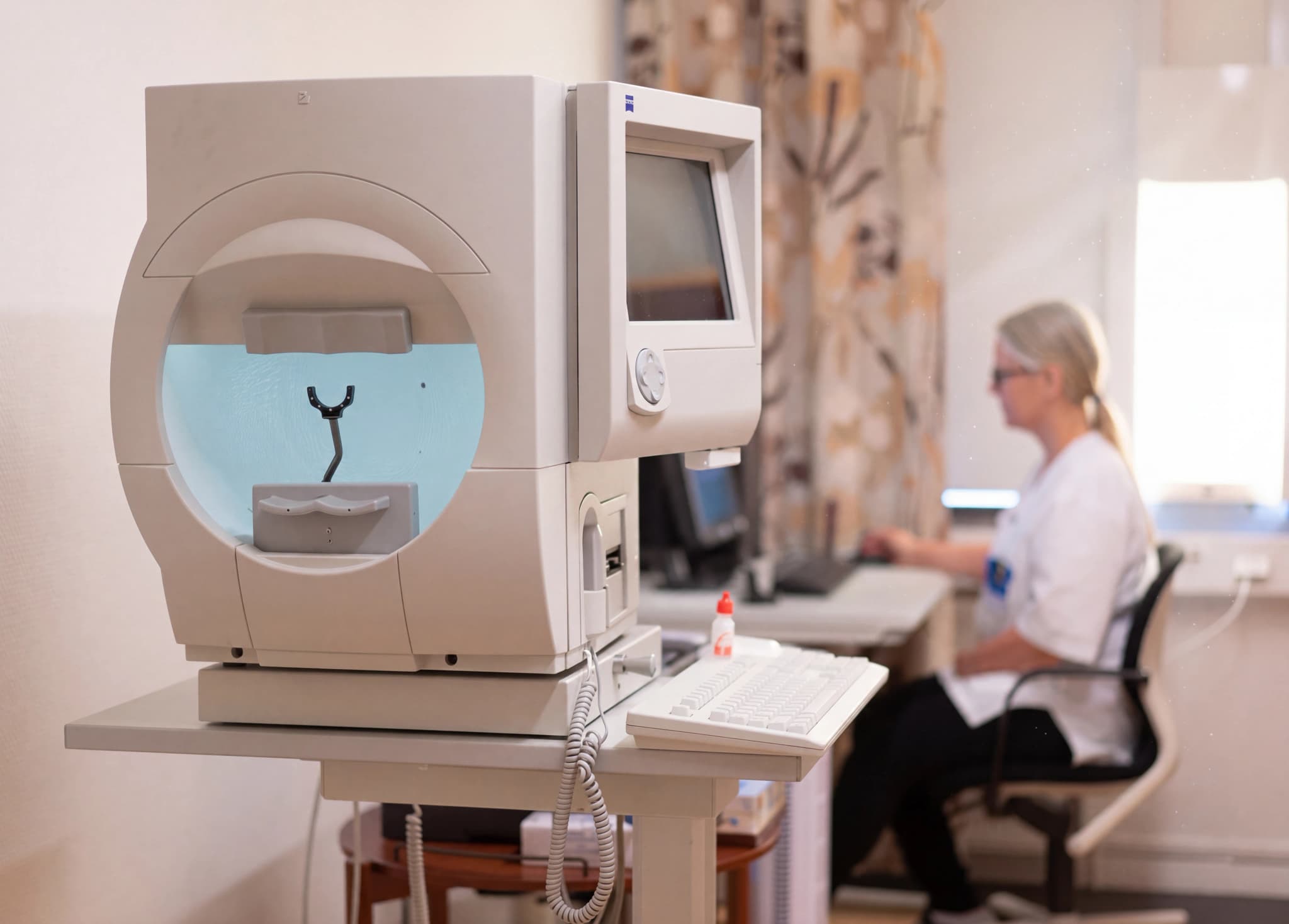 Optiker använder oftalmisk diagnostisk utrustning i ett undersökningsrum.