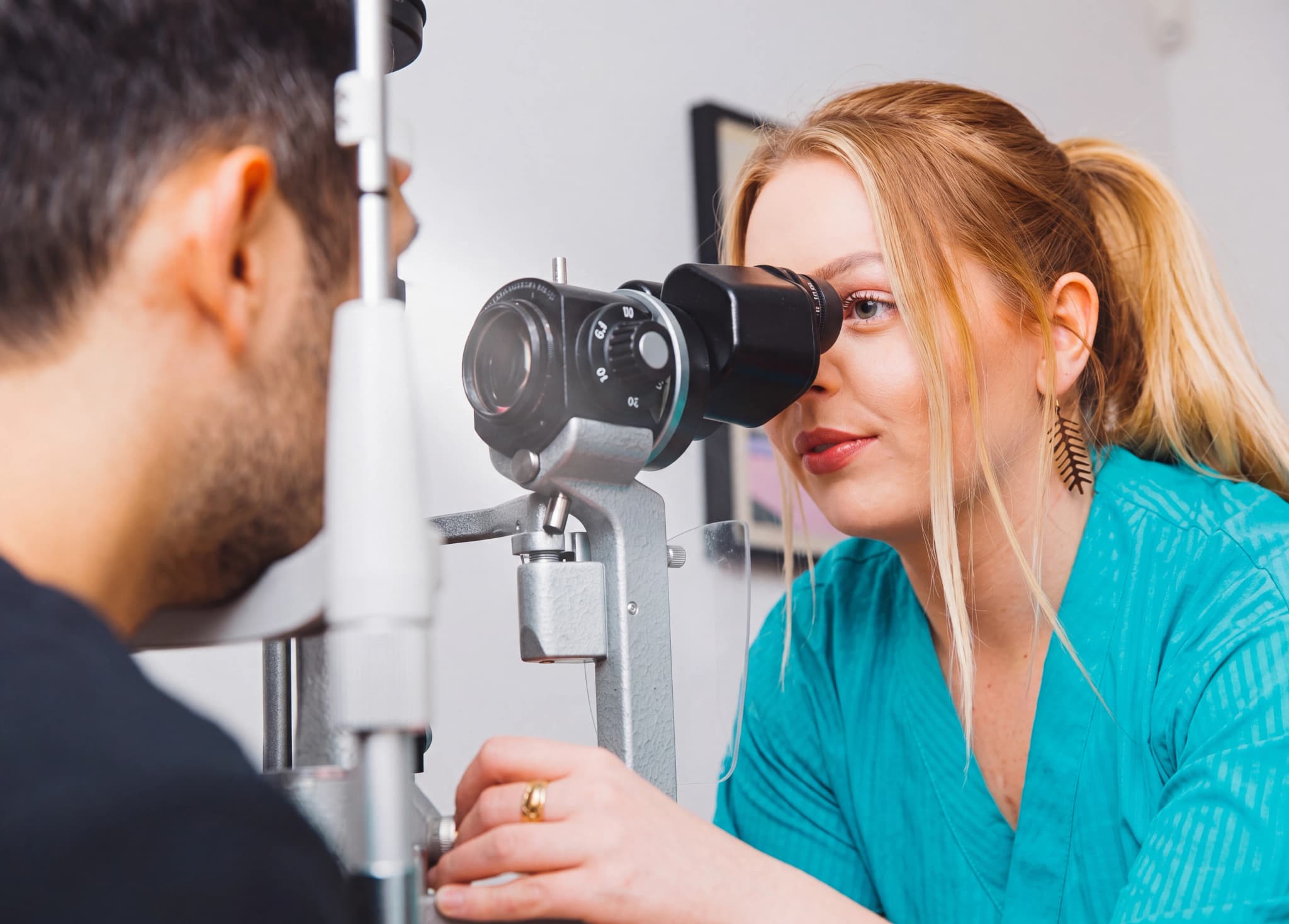 Optiker undersöker en patients öga med en spaltlampa i en undersökningssal.