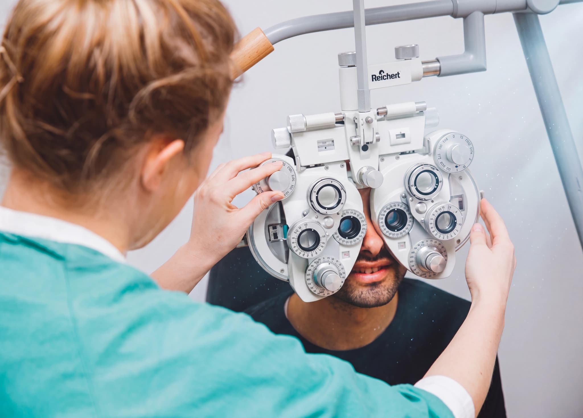 Optiker undersöker patientens ögon med en synundersökningsapparat (phoropter).