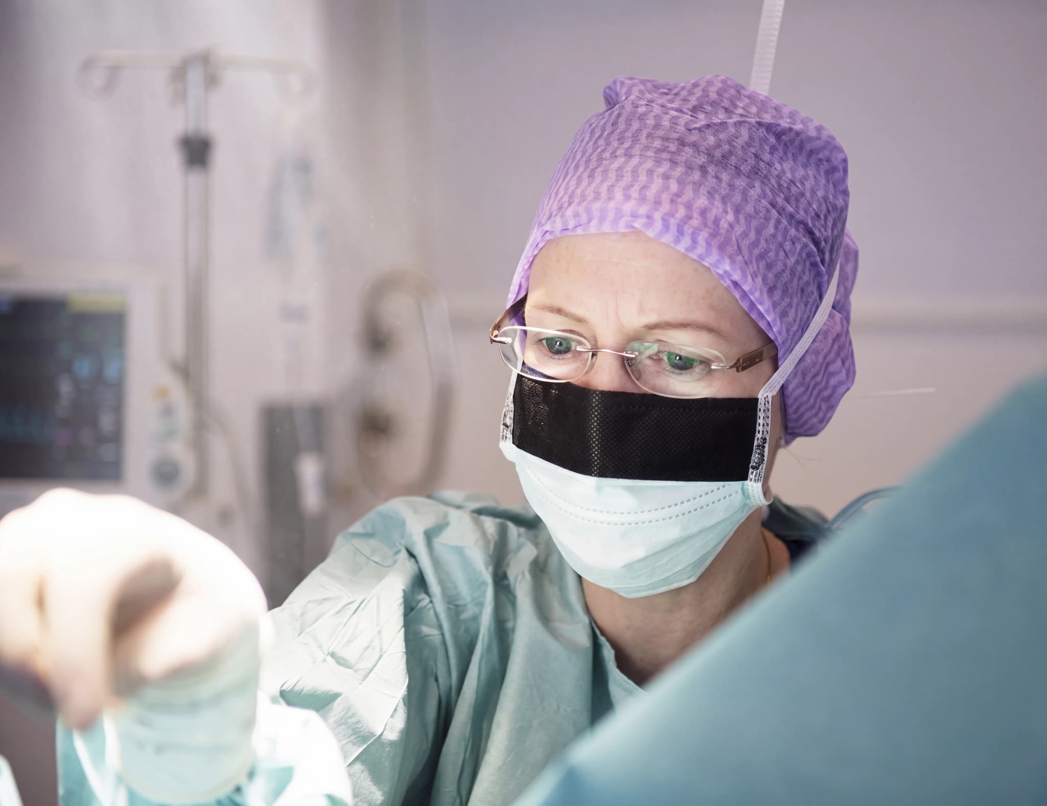 Kirurg klädd i munskydd och operationskläder tittar ner mot ett patientområde.