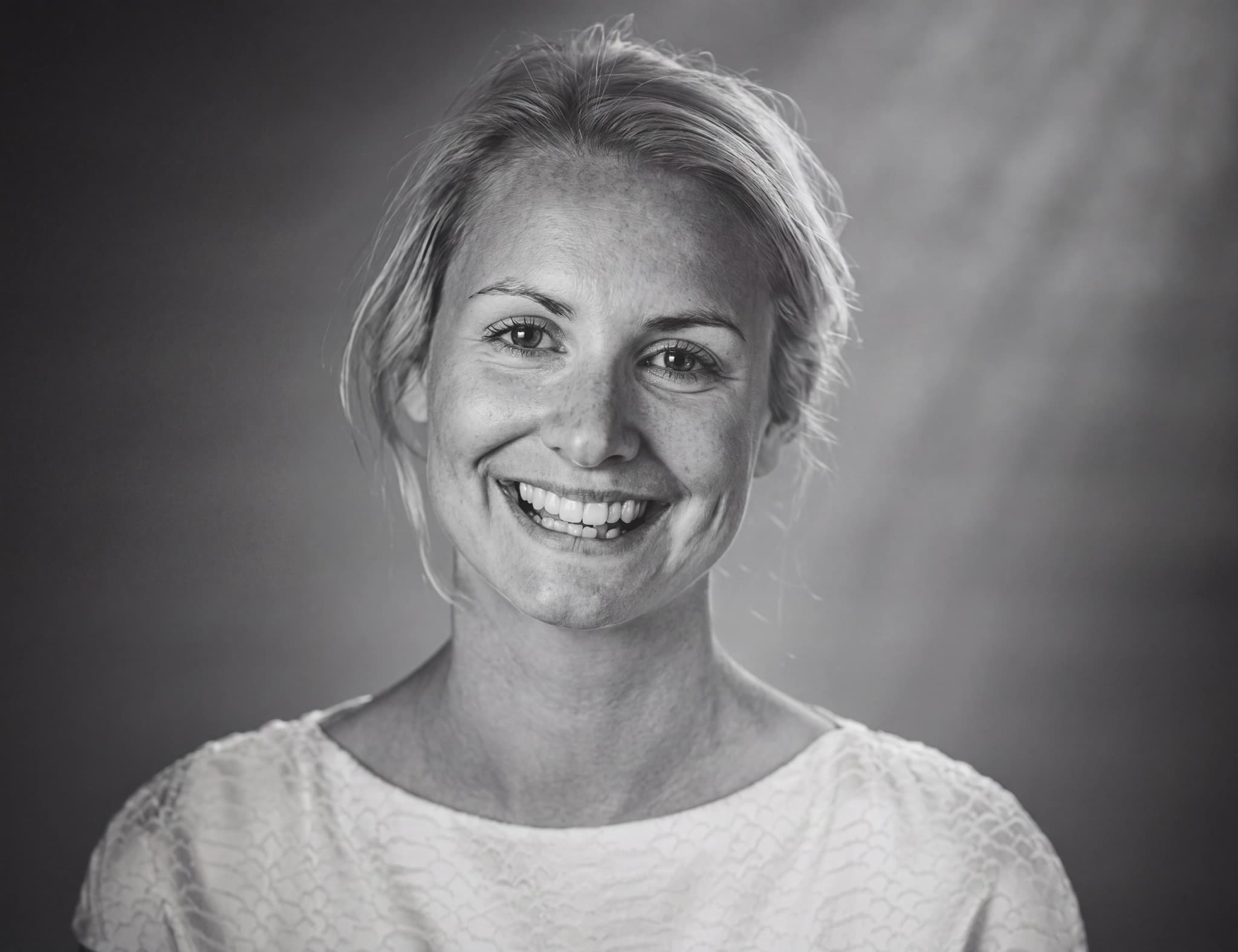 En kvinna med blont hår ler mot kameran i en studiofotografering.