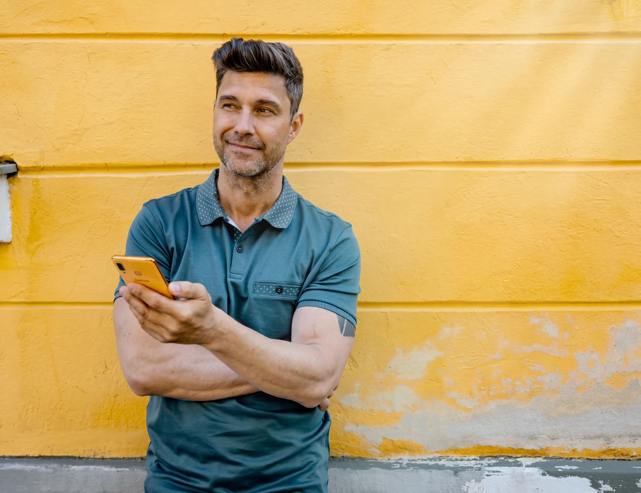 Man i blå polotröja står utomhus med en orange smartphone i handen och tittar bort.