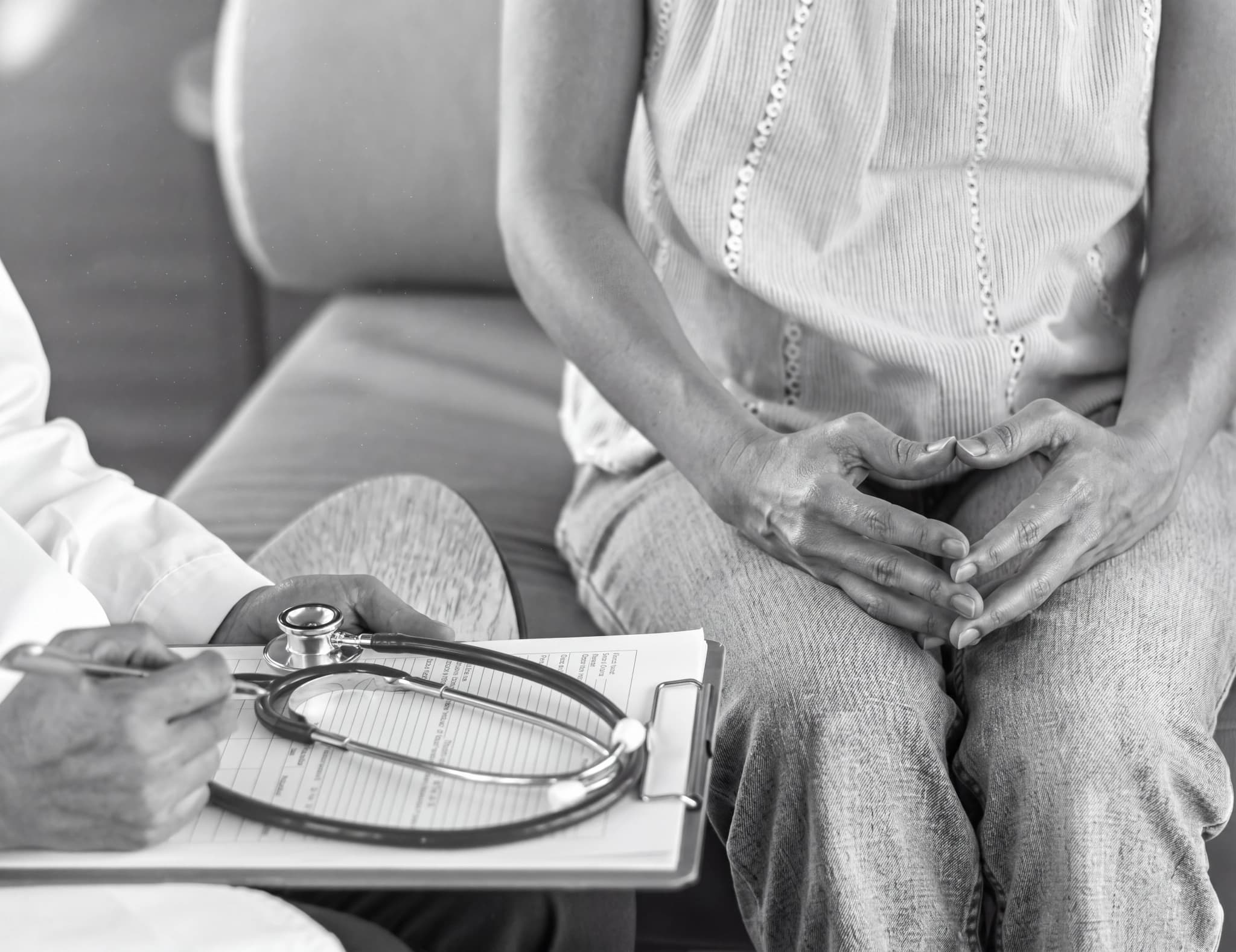 Läkare skriver patientanteckningar med ett stetoskop på ett klippkort framför en patient