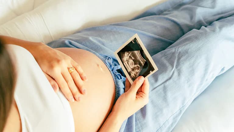 En gravid kvinna ligger ner och håller upp ett ultraljudsbild som visar fostret.