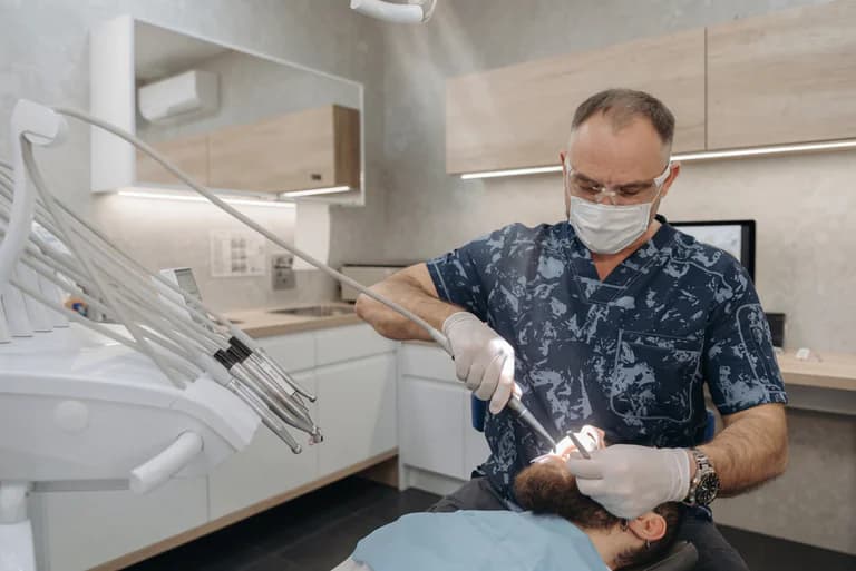Tandläkare i skyddsutrustning undersöker en patients tänder med ett borrutrustning medan patienten ligger i en tandläkarstol.