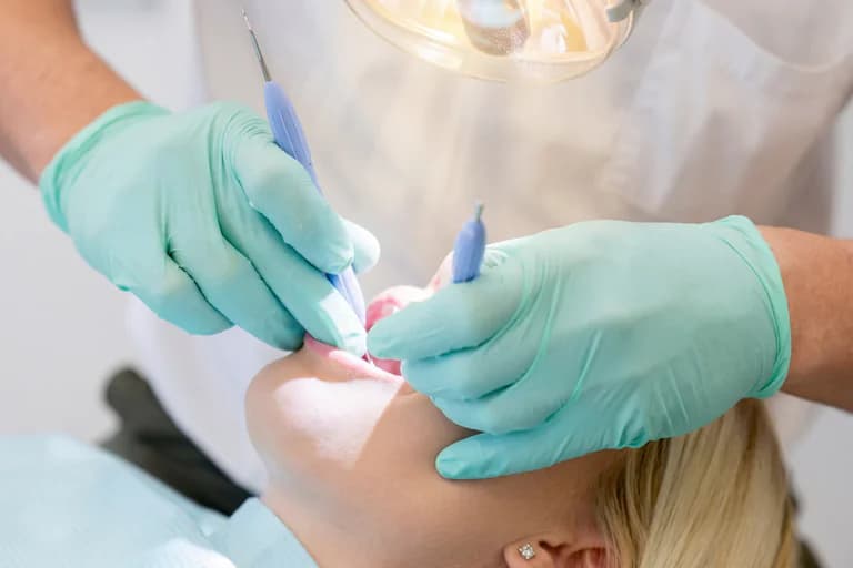 Tandläkare med blå instrument och mintgröna handskar undersöker en patients mun.