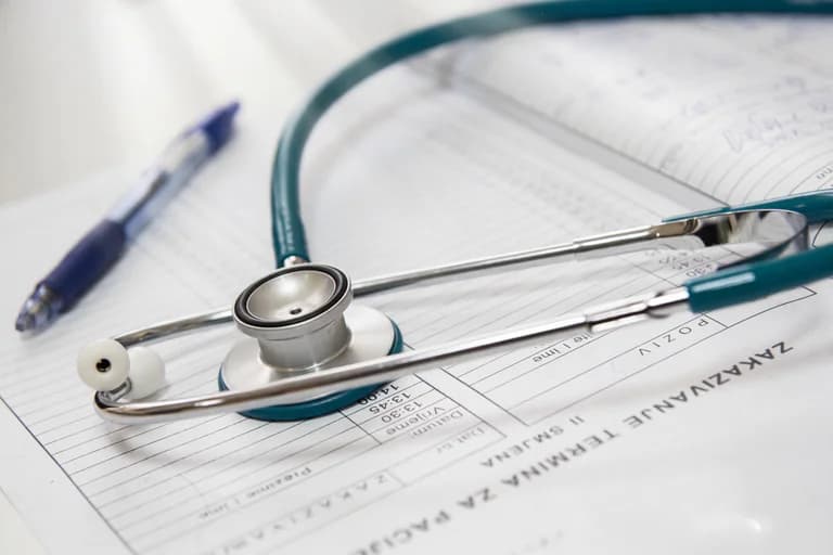 Ett stetoskop och en penna ligger på medicinska formulär.