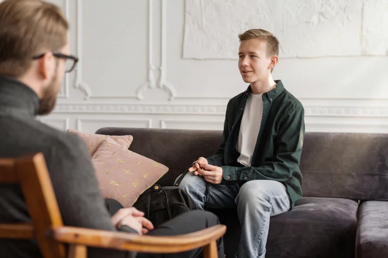 En manlig terapeut sitter i en stol och lyssnar på en tonårspojke som sitter i soffan.