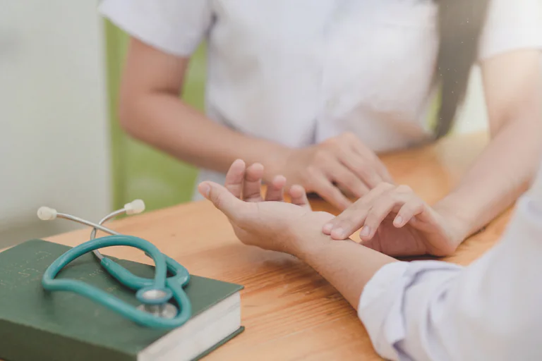 En läkare kontrollerar patientens puls på armen vid ett skrivbord med en bok och ett stetoskop.