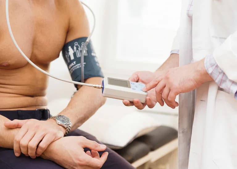 Läkare med vit rock mäter blodtrycket på en manlig patient med en blodtrycksmanschett på armen.
