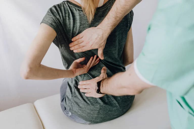 Kiropraktor masserar en patients rygg, sitter på en bänk i en klinik.