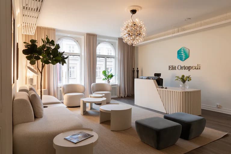 En ljus och modern reception och väntrum på en klinik, med en soffa, fåtöljer, bord och en receptionsdisk.