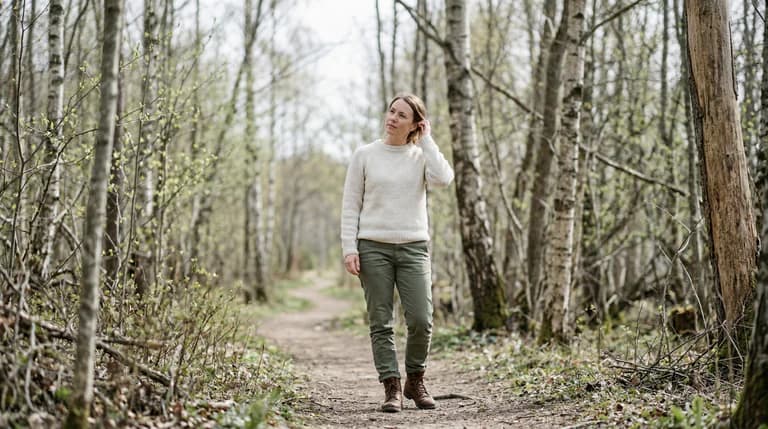 Kvinna i ljus tröja och gröna byxor går på en stig i en skog på våren.