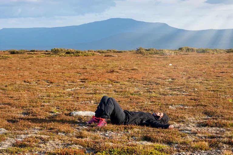 Person ligger avslappnat på gräsmark med berg i bakgrunden.