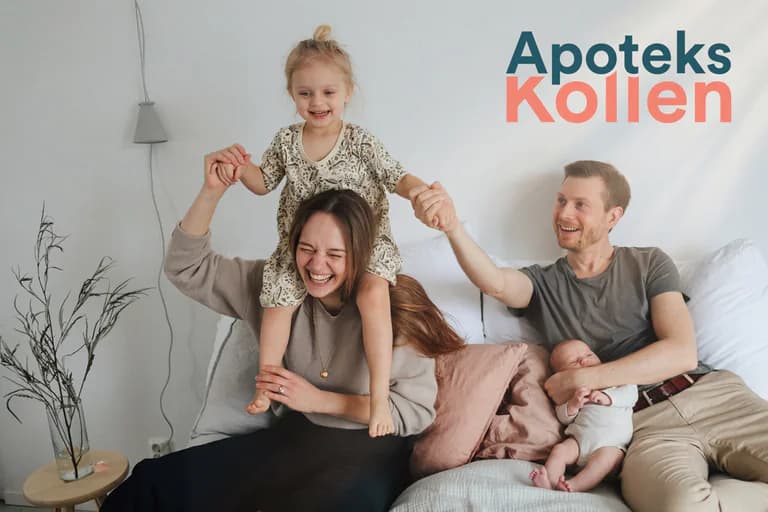 En leende familj med två barn sitter på en soffa hemma, med en baby i famnen och en flicka som sitter på mammas axlar.