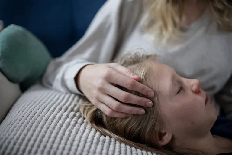 En mamma håller handen på sitt sovande barn i sängen.