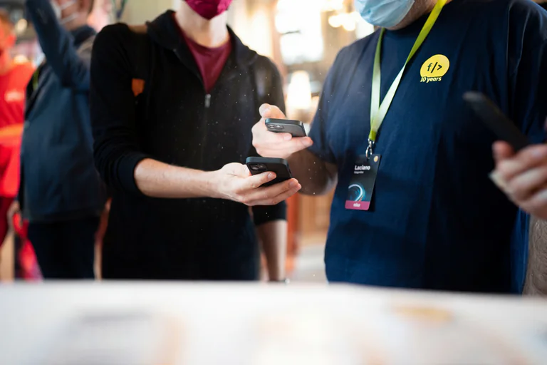 Två personer med ansiktsmasker som tittar på sina smartphones på ett evenemang.