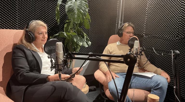 Två personer sitter i hörlurar med mikrofoner framför sig i en ljudisolerad studio.