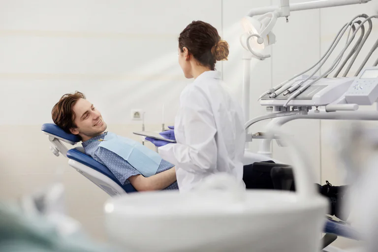 En tandläkare i vit rock diskuterar med en patient som ligger i en tandläkarstol.