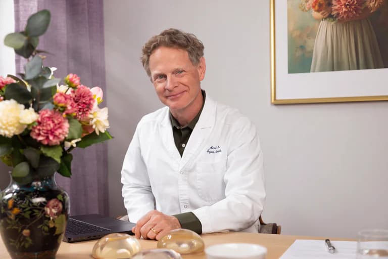 Man i läkarrock sitter vid ett skrivbord med en blomsterbukett och medicinska implantat