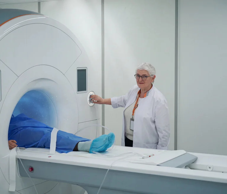 Läkare med vit rock trycker på kontrollpanelen på en MR-skanner medan en patient ligger inuti.