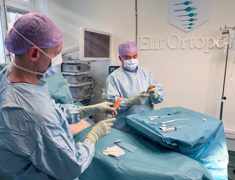 Två kirurger i operationskläder och skyddsutrustning förbereder sig för en stamcellsbehandling, med instrument och injektionssprutor framlagda.
