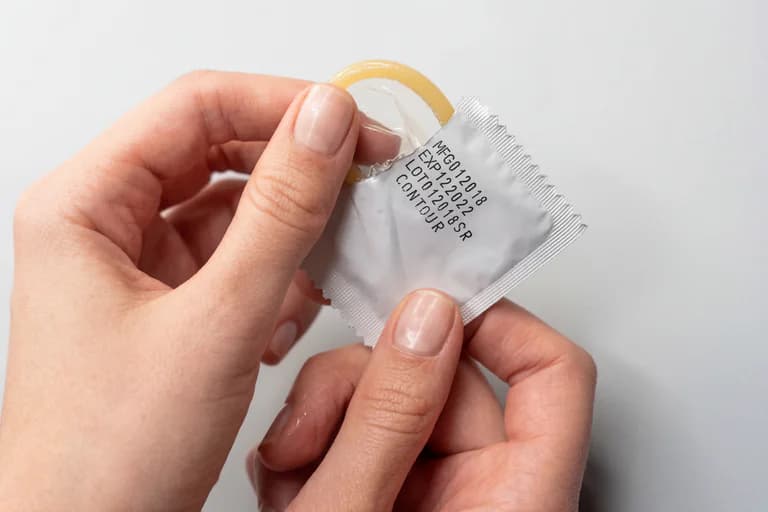 Händer öppnar en förpackning med ett kondom. Datum för tillverkning och utgångsdatum syns på förpackningen.