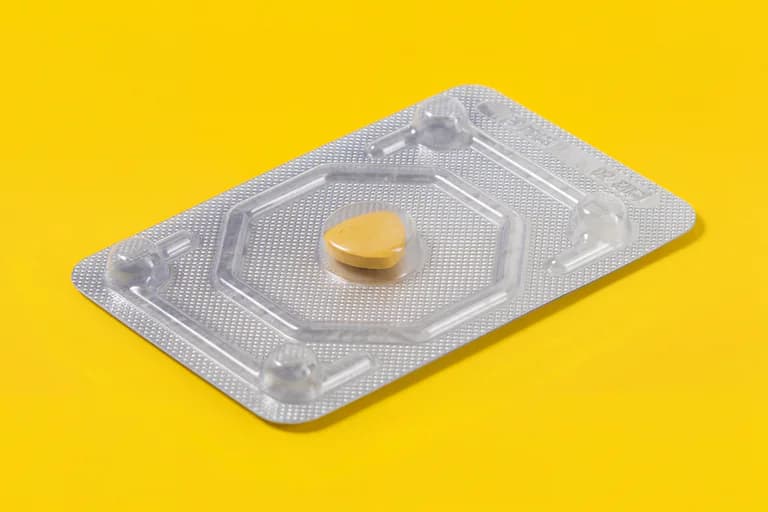 En orange tablett i en genomskinlig blisterförpackning på en gul bakgrund.